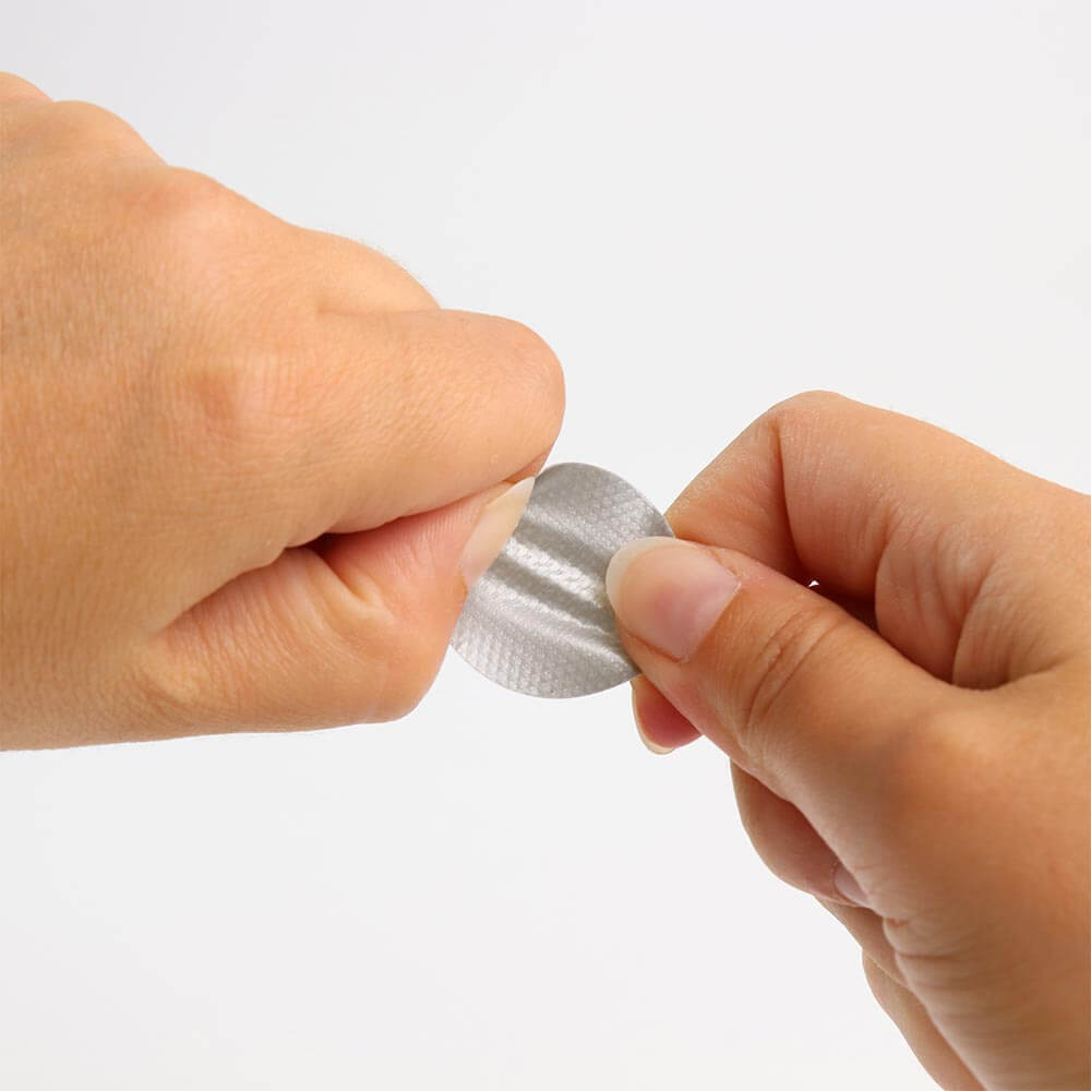 Zwei H&auml;nde ziehen einen silbernen Gewebeklebepunkt &ndash; das flexible und formbest&auml;ndige Material passt sich ideal an unebene Oberfl&auml;chen an.
