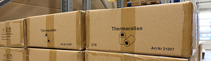 Gestapelte Kartons mit der Aufschrift „Thermorollen“ in einem Lagerraum, die die empfohlene Lagerung in Originalverpackung veranschaulichen.