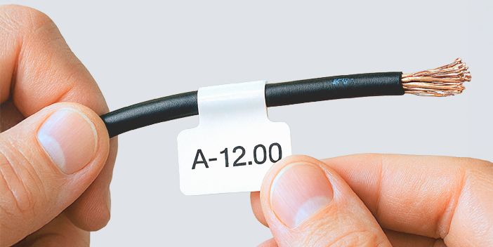 Nahaufnahme eines schwarzen Elektrokabels, das von zwei Händen gehalten wird. An dem Kabel ist eine weiße Kabelfahne mit dem Text „A-12.00“ angebracht.