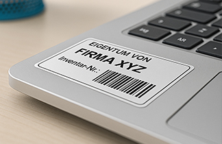 Laptop mit Eigentumsetikett zur Inventarisierung, beschriftet mit Firmenname, Inventarnummer und Barcode.